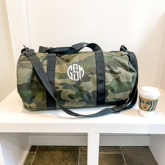 camo duffle with monogram sitting on bench with starbucks cup sitting beside it