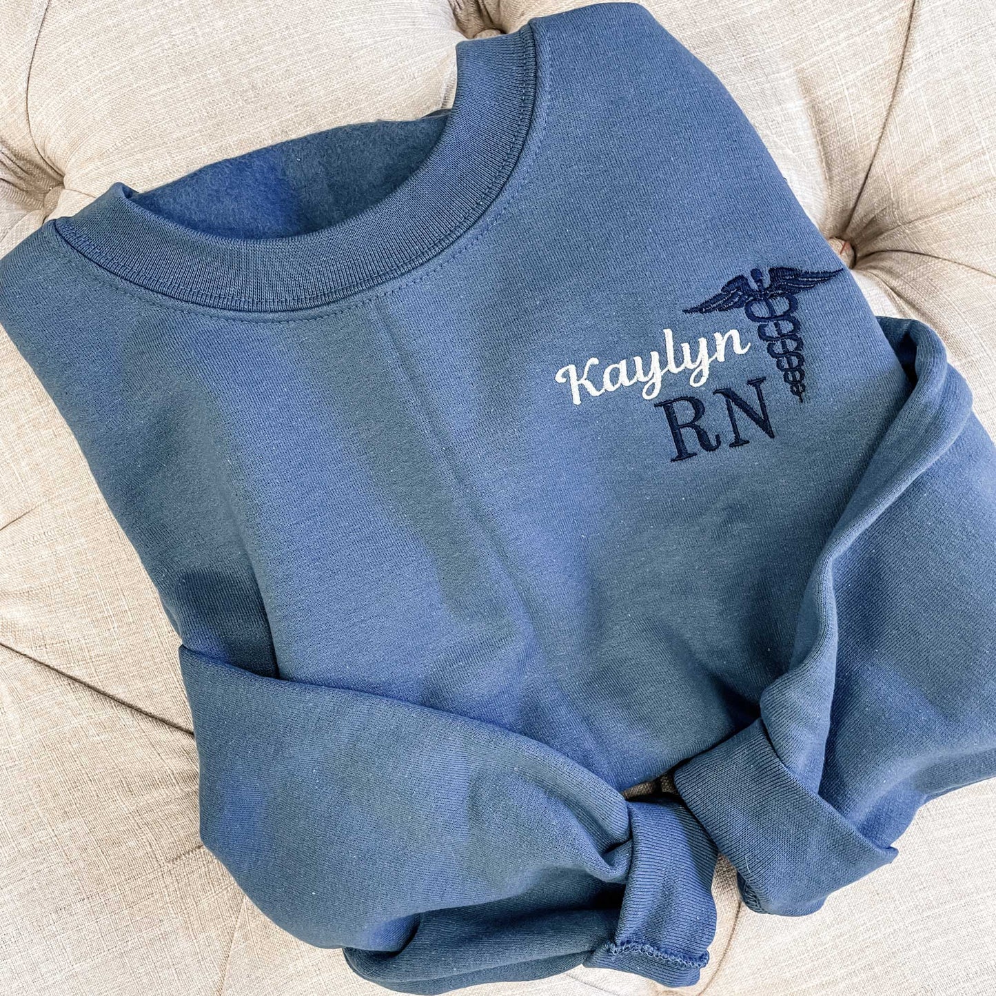 folded indigo blue crewneck sweatshirt with a personalized nurse embroidery design on the left chest