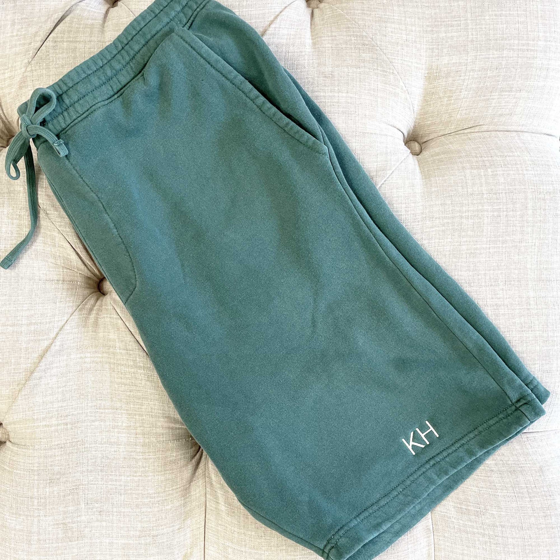 a pair of green lounge shorts folded on an ottoman featuring a mini monogram stitched near the lower hemline of the left leg