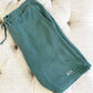 a pair of green lounge shorts folded on an ottoman featuring a mini monogram stitched near the lower hemline of the left leg