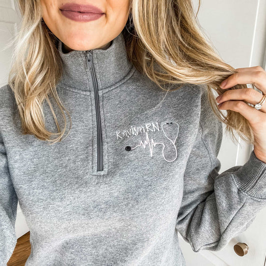 woman wearing a collared quarter zip pullover sweatshirt featuring a custom nurse embroidery design on the left chest