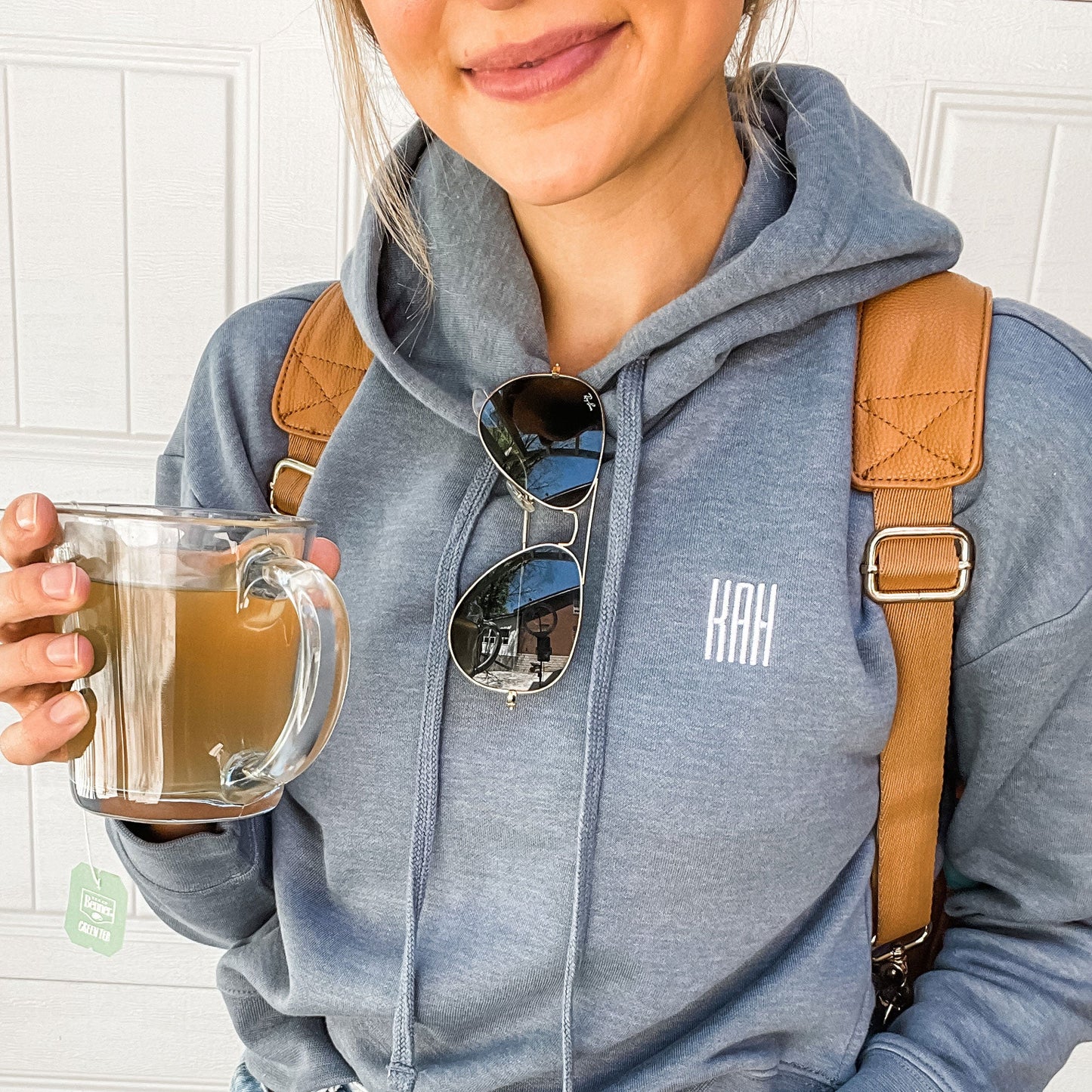 woman carrying backpack and tea mug sporting blue embroidered hoodie