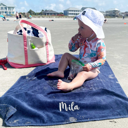 toddler sitting on a personalized blue bleach towel on the beach