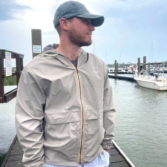 man standing on a boat deck wearing a full zip vintage style khaki rain jacket personalized with a staggered two-letter monogram