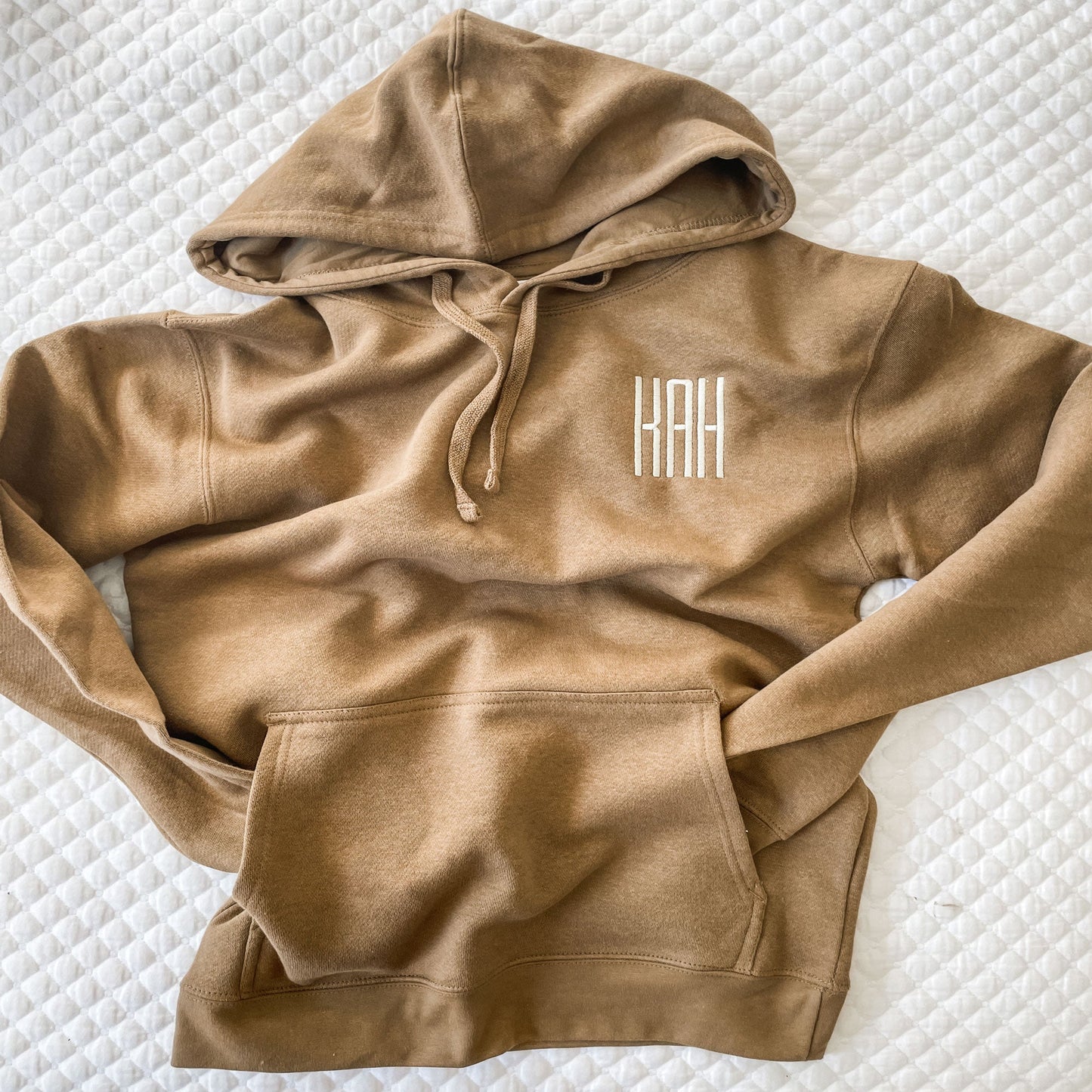 full photo of a hooded pullover sweatshirt in a warm brown tone with a three letter monogram on left chest