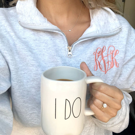 Close up of woman wearing a light gray quarter zip sweatshirt  with a custom script monogram embroidered 