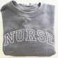close up of a graphite heather crew with an embriodered NURS design