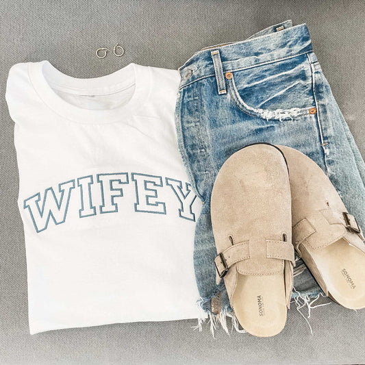 outfit layout featuring an embroidered white tee with wifey embroidered in an open block athletic font