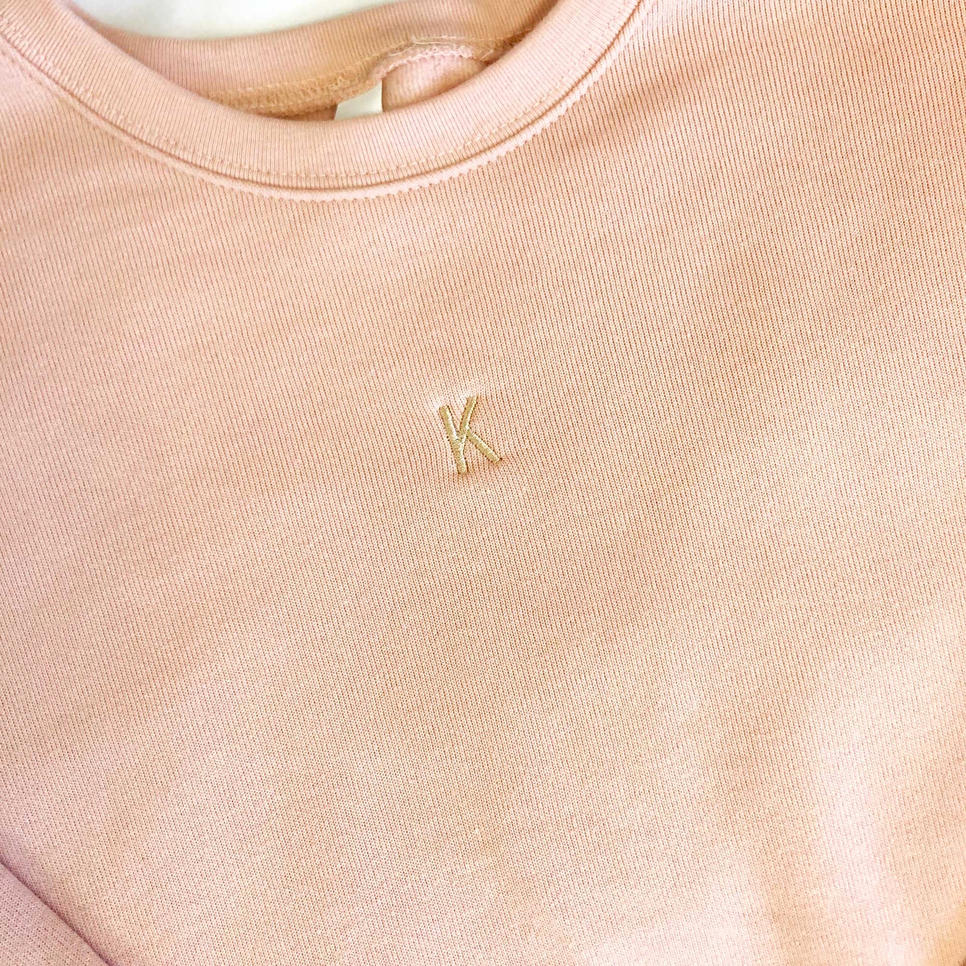 close up of mini one letter personalized embroidery on a peach crewneck bella and canvas sweatshirt