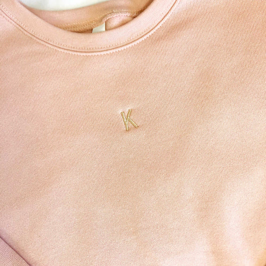 close up of mini one letter personalized embroidery on a peach crewneck bella and canvas sweatshirt