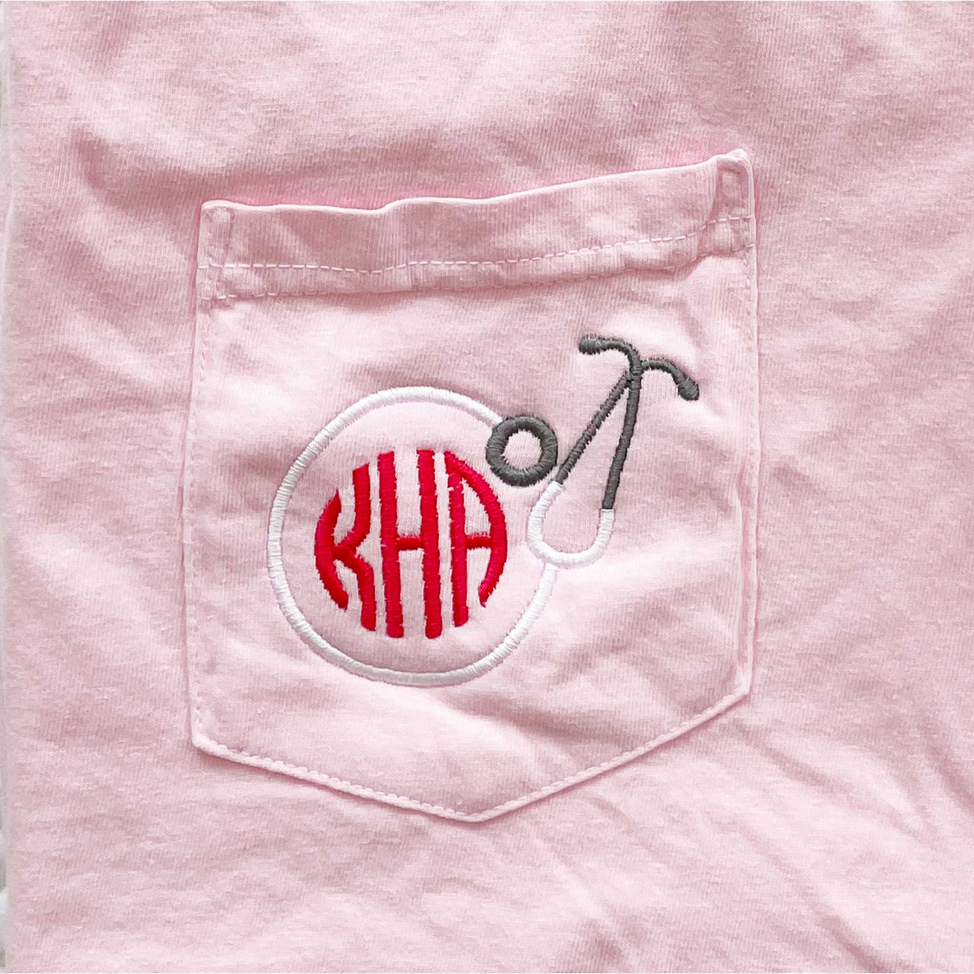 close up of a custom round stethoscope and three letter monogram design embroidered on the pocket of a t-shirt