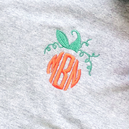 close up of a custom monogram embroidery styled as a pumpkin with a stem and curling vines above the rounded three letter monogram