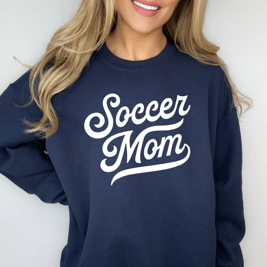 woman wearing a navy blue pullover sweatshirt with soccer mom printed across the chest in a varsity script font 
