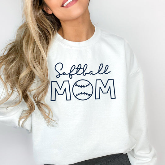 woman wearing a white sweatshirt featuring a printed design reading 'softball' in a script font and 'mom' in an open block font with a baseball in place of the 'o'