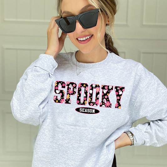 woman wearing an ash crewneck sweatshirt with a custom colorful daisy and ghost pattern print reading "spooky season'