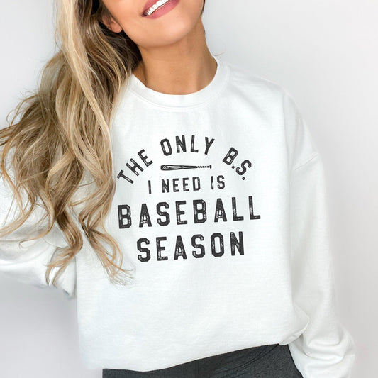 woman wearing an oversized white sweatshirt with a distressed print in black ink reading 'the only b.s. i need is baseball season'