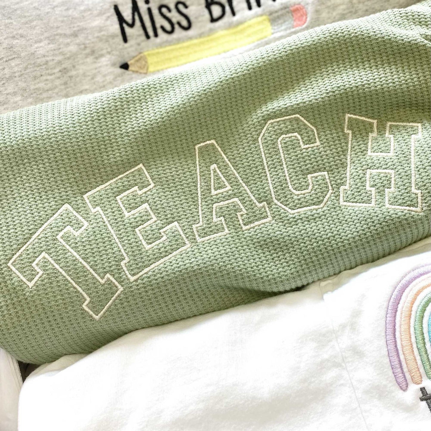 close up of embroidered teach open athletic block design on a sage green waffle knit crew