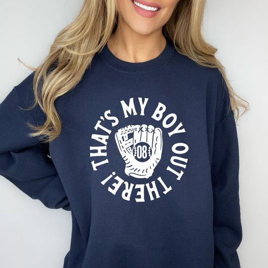 woman wearing a navy blue crewneck sweatshirt with a printed design of a baseball mitt with player number in the center and 'that's my boy out there!' in a circle around it.
