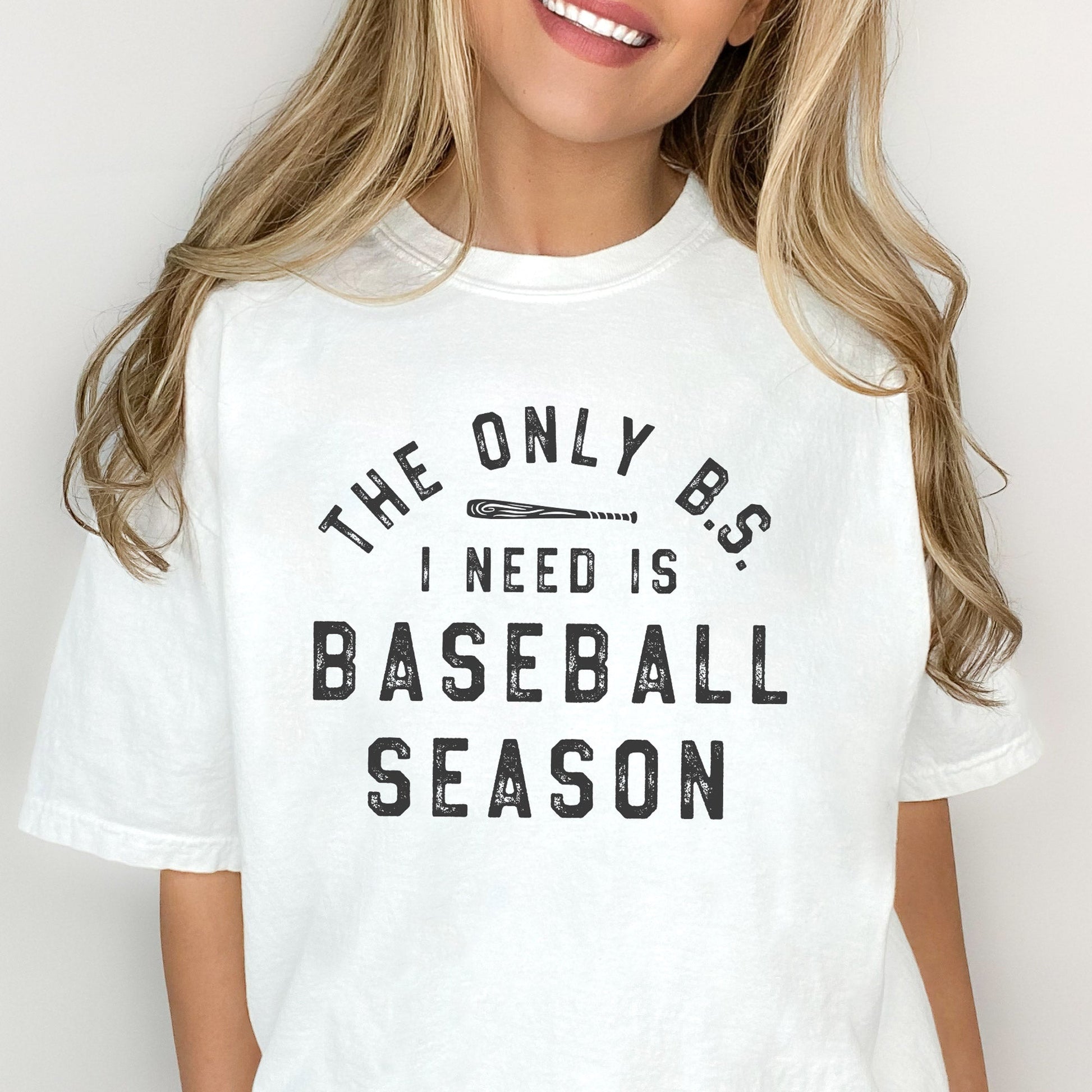 woman wearing an oversized white t-shirt featuring a distressed printed design reading 'the only b.s. i need is baseball season'