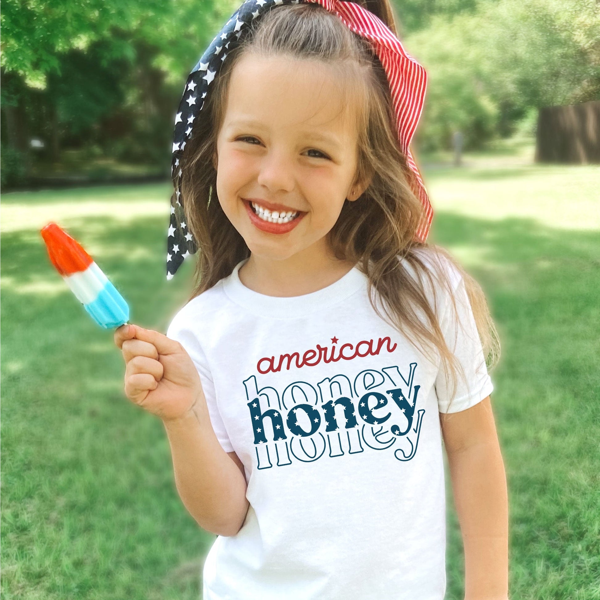 little girl wearing a white t-shirt with a red white and blue printed design reading 'american honey' across the chest