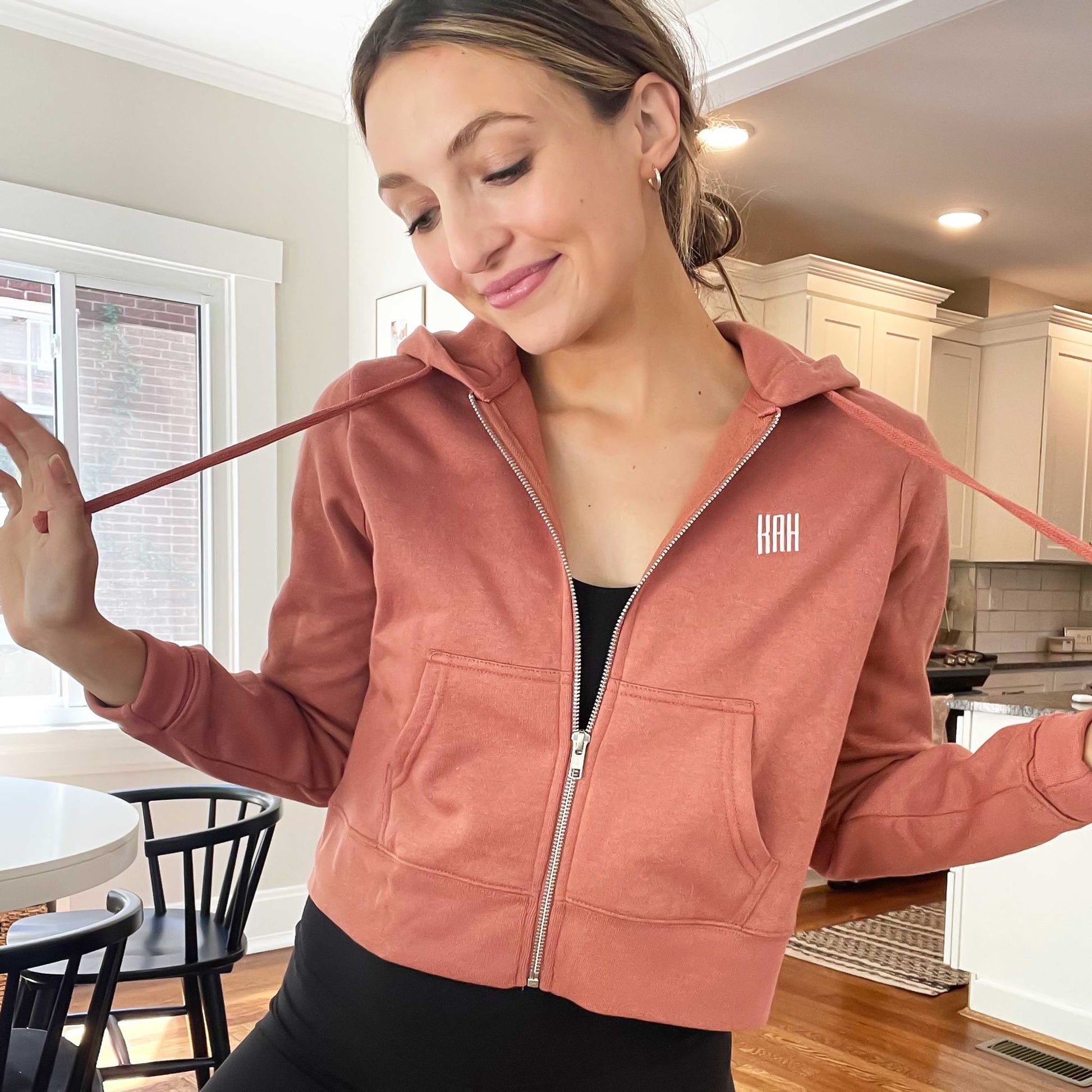 woman wearing a cropped desert rose full zip jacket with mini monogram embroidery detail over a athletic bodysuit