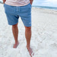 man standing on the beach and wearing a pair of casual sweat shorts with a custom two-letter monogram embroidered near the lower hem of the left leg 