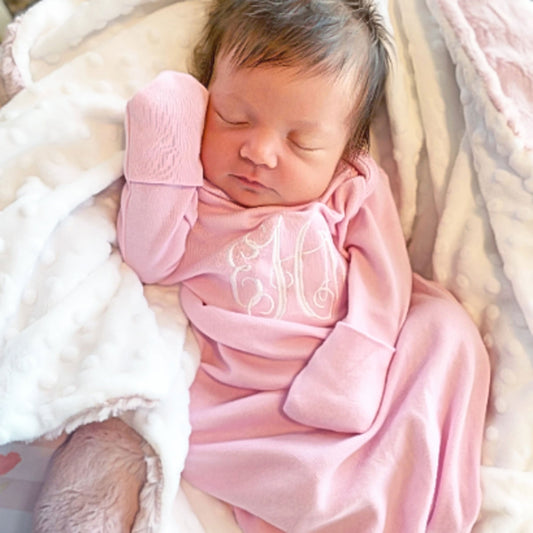 sleeping baby with dark hair wearing light pink layette with white embroidery