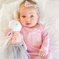 baby girl snuggling with toy bunny wearing pale pink layette with monogram embroidered on chest