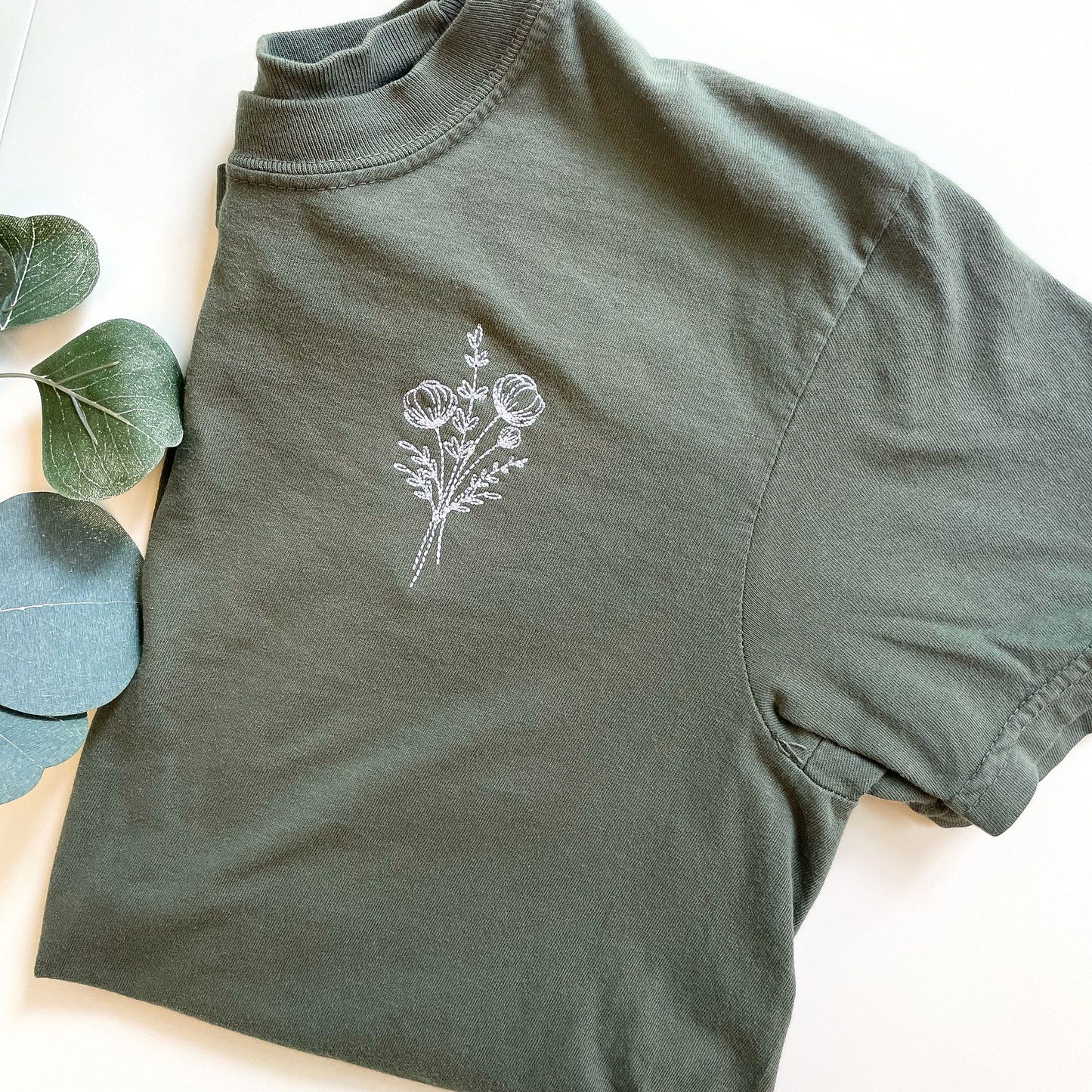 green comfort colors t-shirt with an outlined flower embroidery design on the left chest