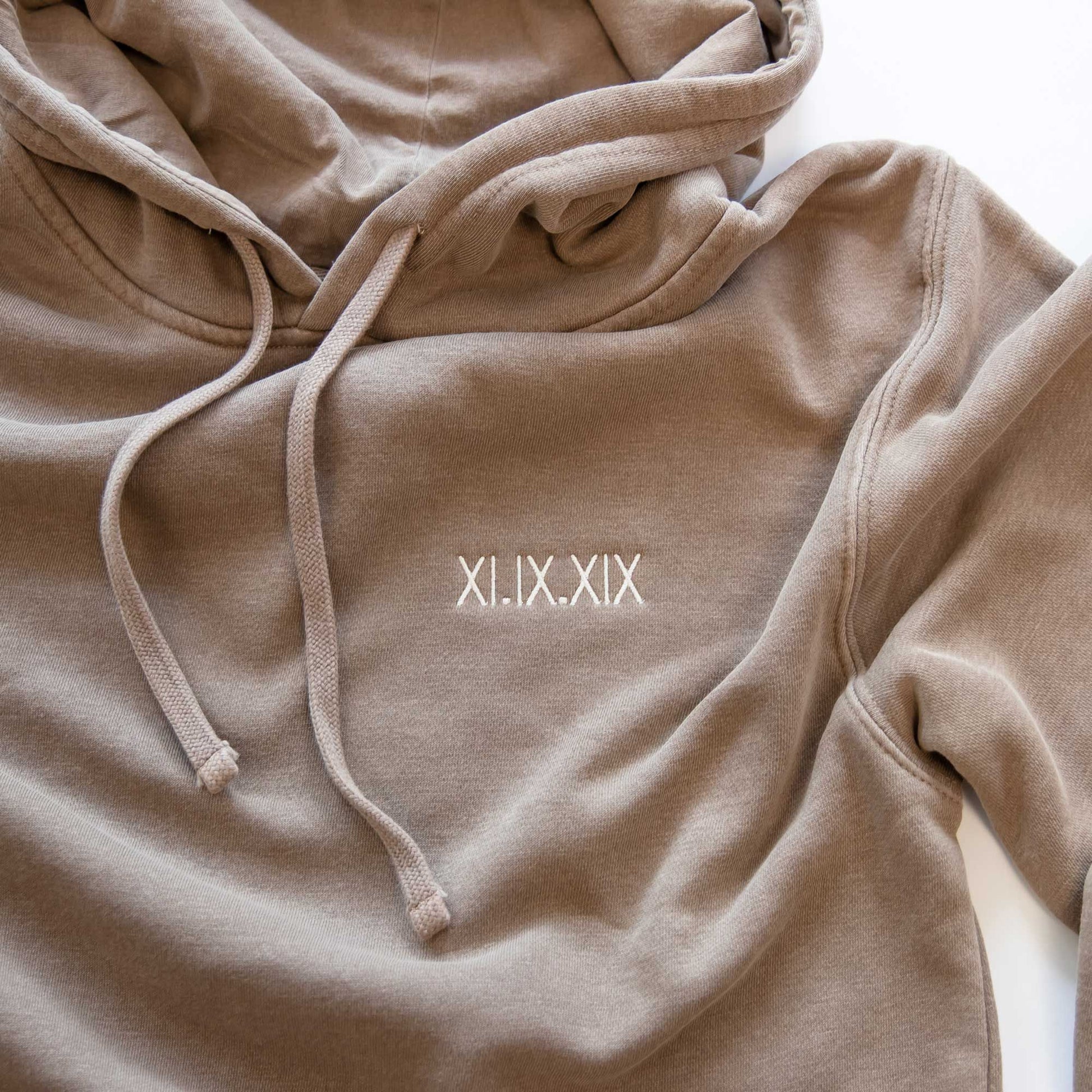 flat image of a vintage brown hooded sweatshirt with a personalized mini roman numeral embroidered design on the left chest in a natural thread