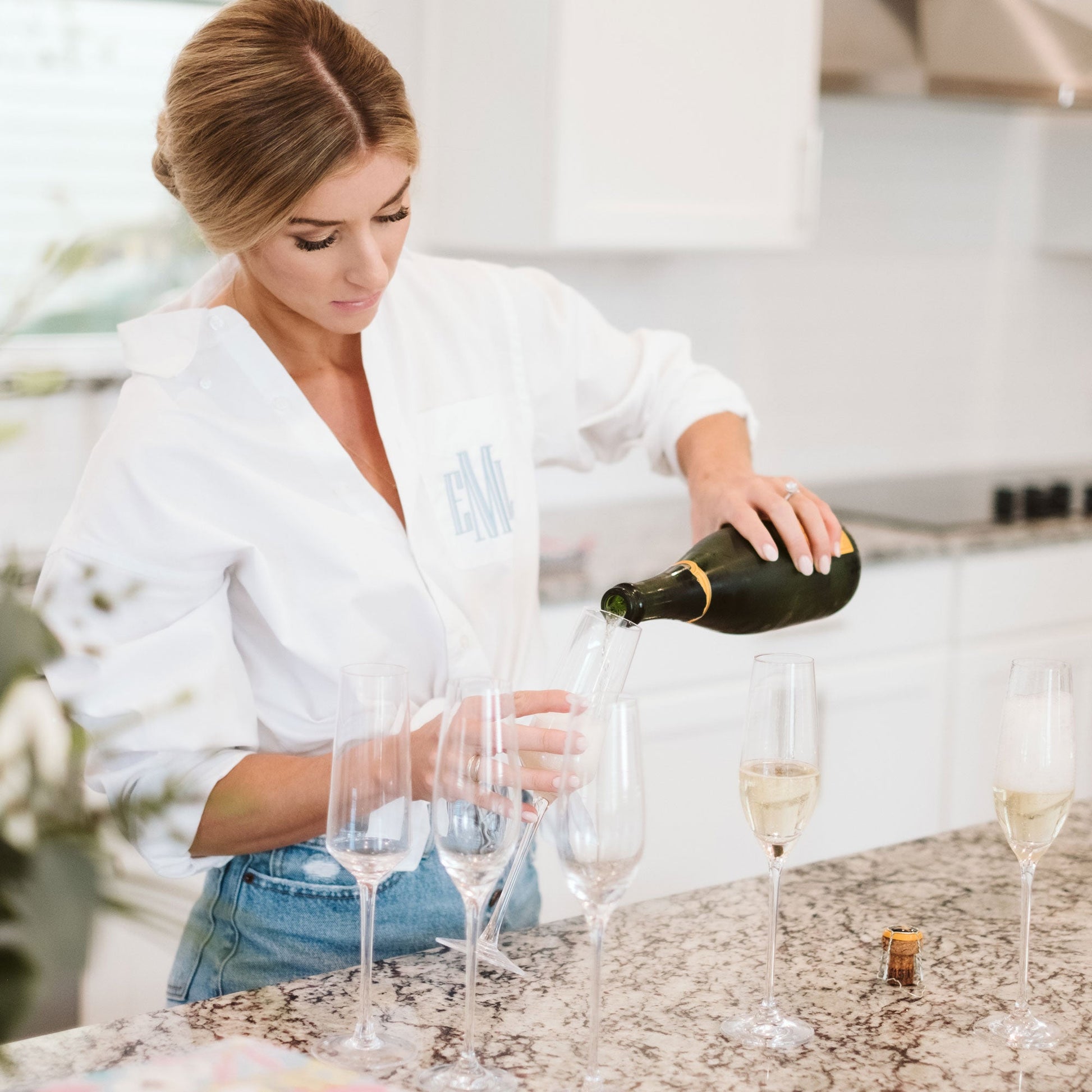 bride pouring a glass of champagne wearing a white dress shirt with personalized embroidery in light blue thread on the pocket 