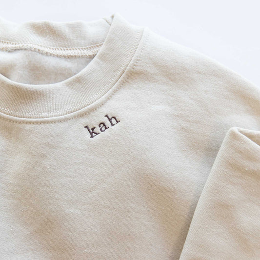 clos up of a a sand crewneck sweatshirt with embroidered mini initials in all lowercase kah on the neckline in java thread