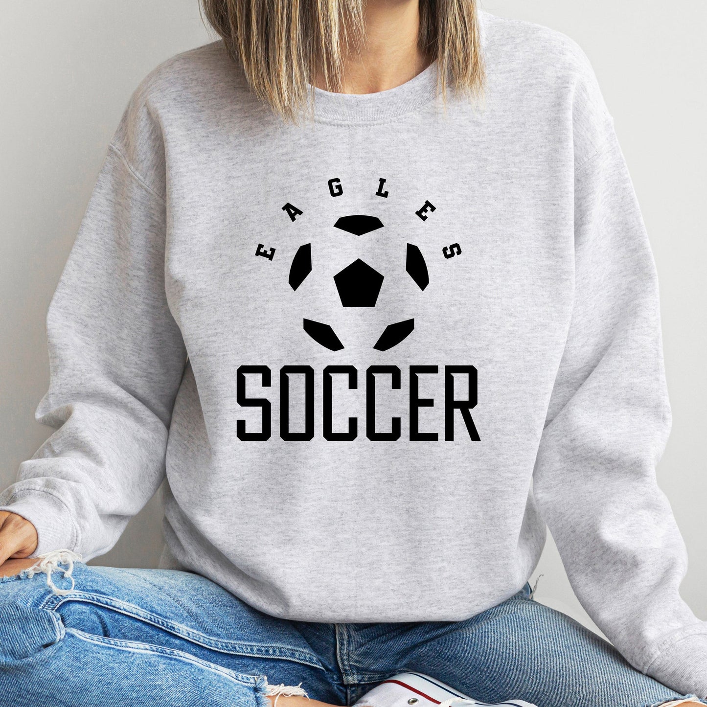 woman wearing a custom dtg printed sweatshirt featuring a soccer ball, the word soccer, and the mascot or team name. 