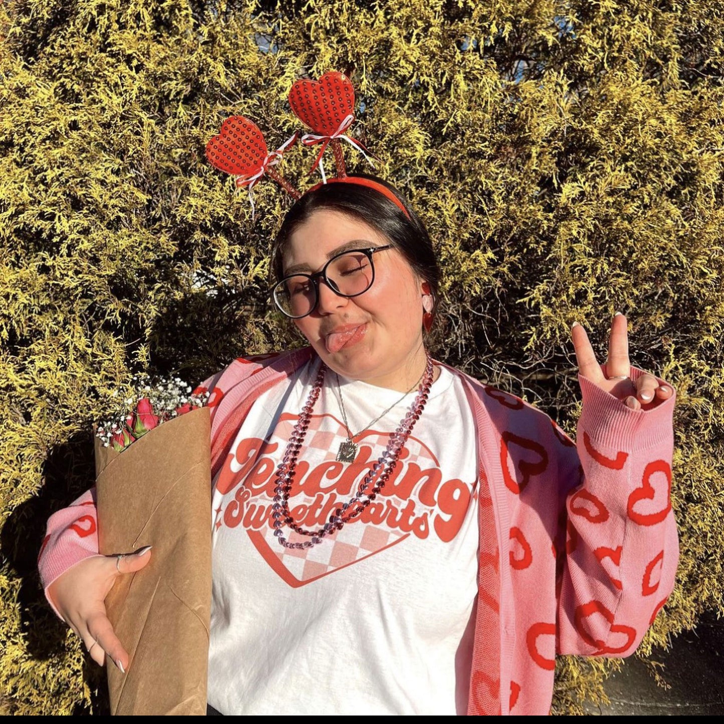 woman styling a teaching sweethearts pint t-shirt holding flowers and wearing fun valentine's accessories